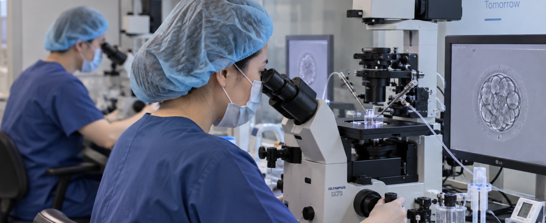 AI-generated embryologists working at microscopes in an IVF laboratory, with an embryo image on a monitor.